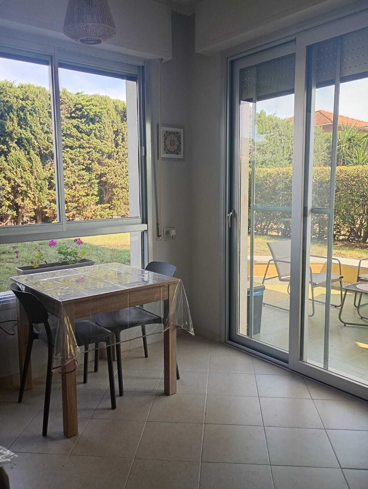 Zona pranzo con tavolo e sedie, ampie finestre e vista sul verde circostante.