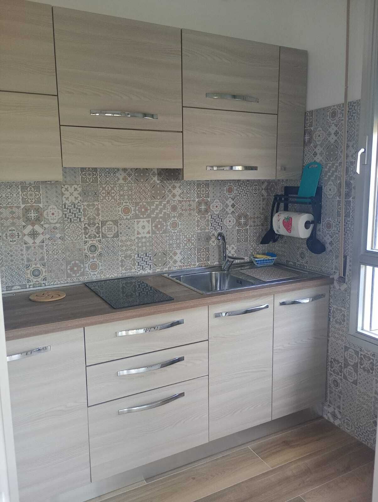 A kitchen with light wood cabinets, a stainless steel sink, and patterned backsplash tiles.