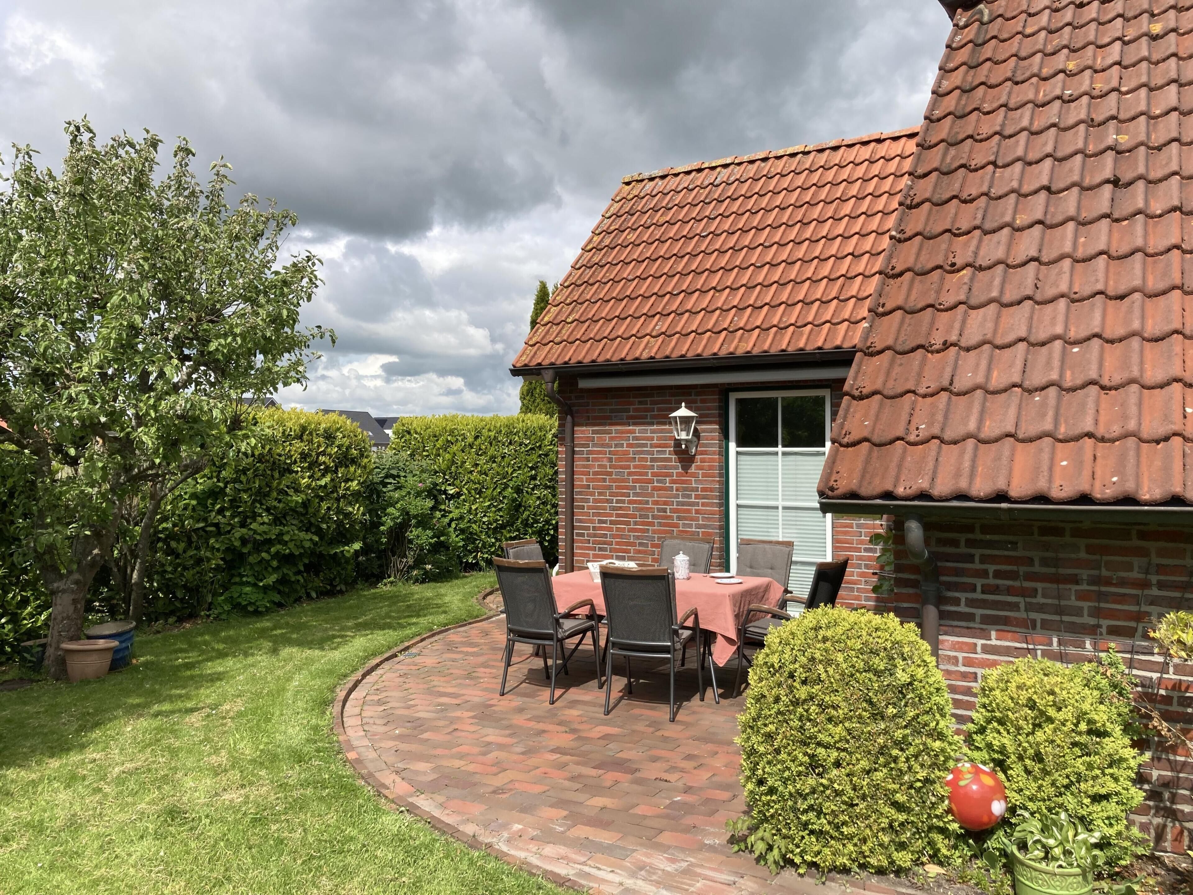 Et murstenshus med et tegltag, en terrasse med bord og stole, og en velplejet have.