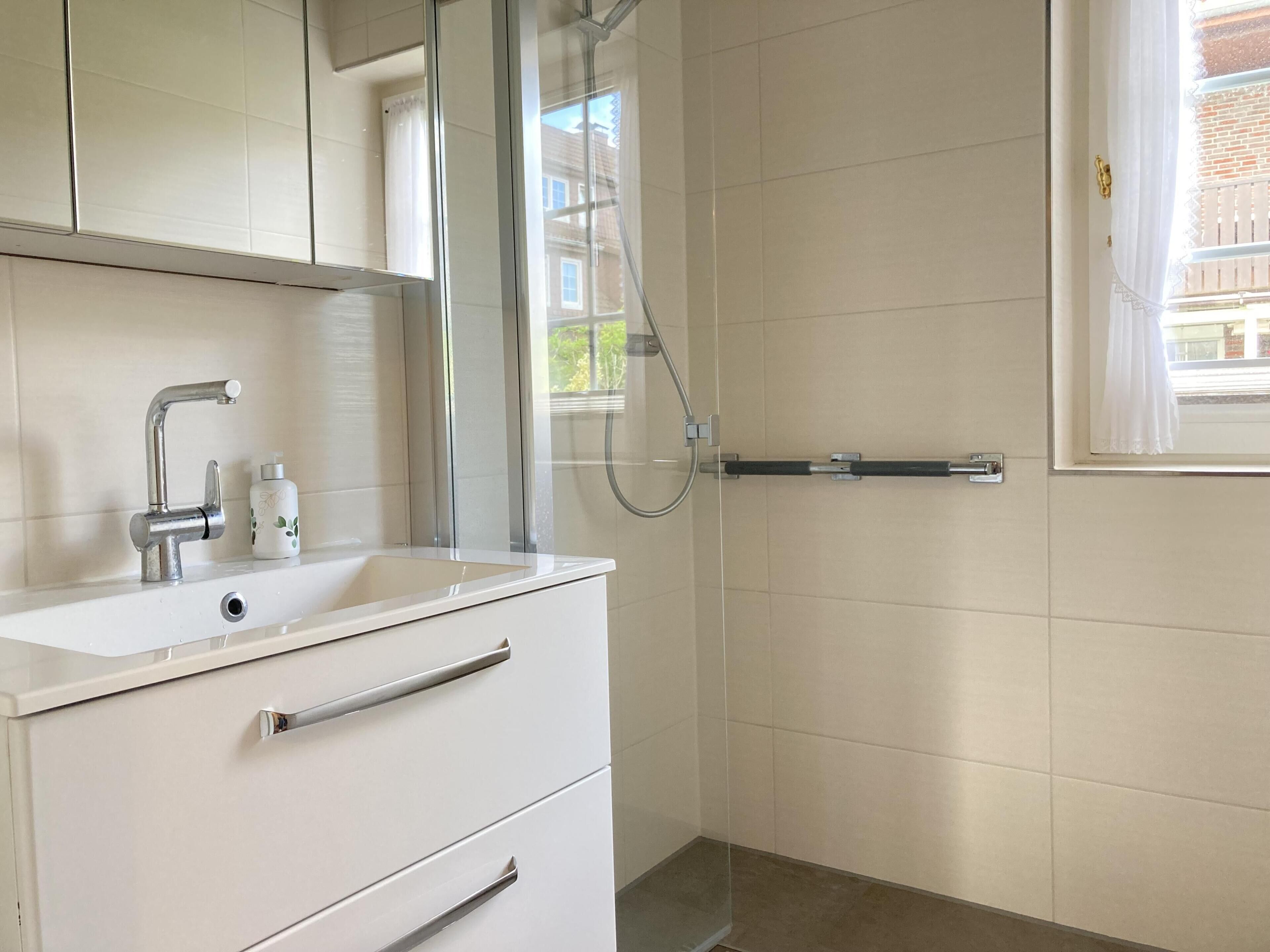 A bathroom with a white sink, a mirror, a shower, and a window.