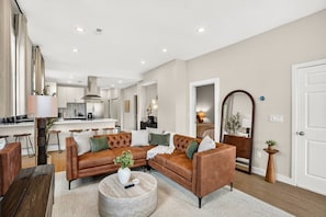 A modern living room with a brown leather sofa, a round coffee table, and a kitchen in the background.