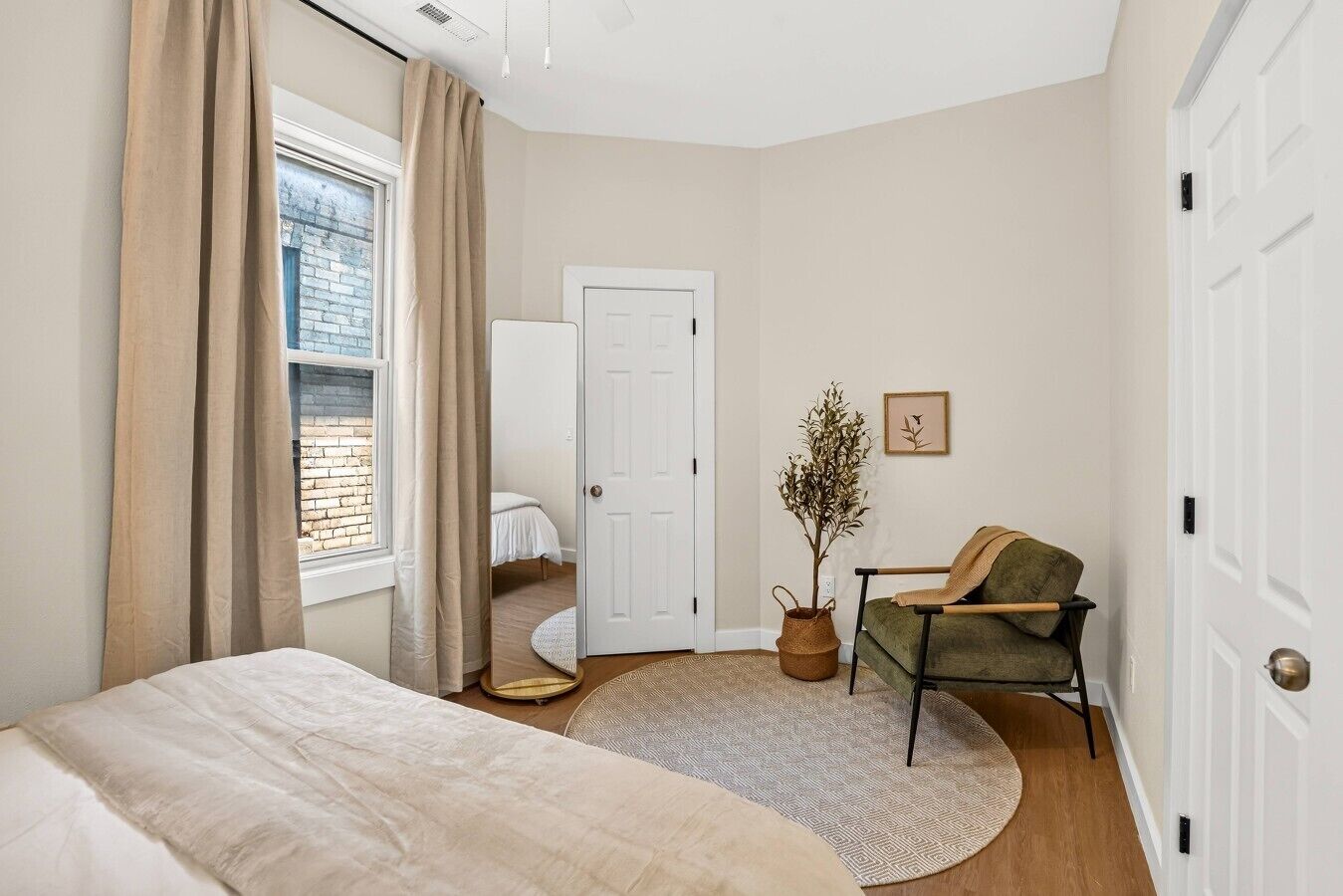 A bedroom with a bed, a chair, a potted plant, a door, and a window with curtains.