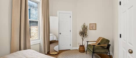 A bedroom with a bed, a chair, a potted plant, a door, and a window with curtains.