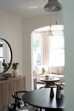 A dining area with a round table, chairs, a mirror, and a hanging light fixture.