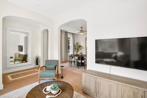 A spacious living room with a large flat-screen TV, a dining area with a table and chairs, and a seating area with a sofa and armchairs.