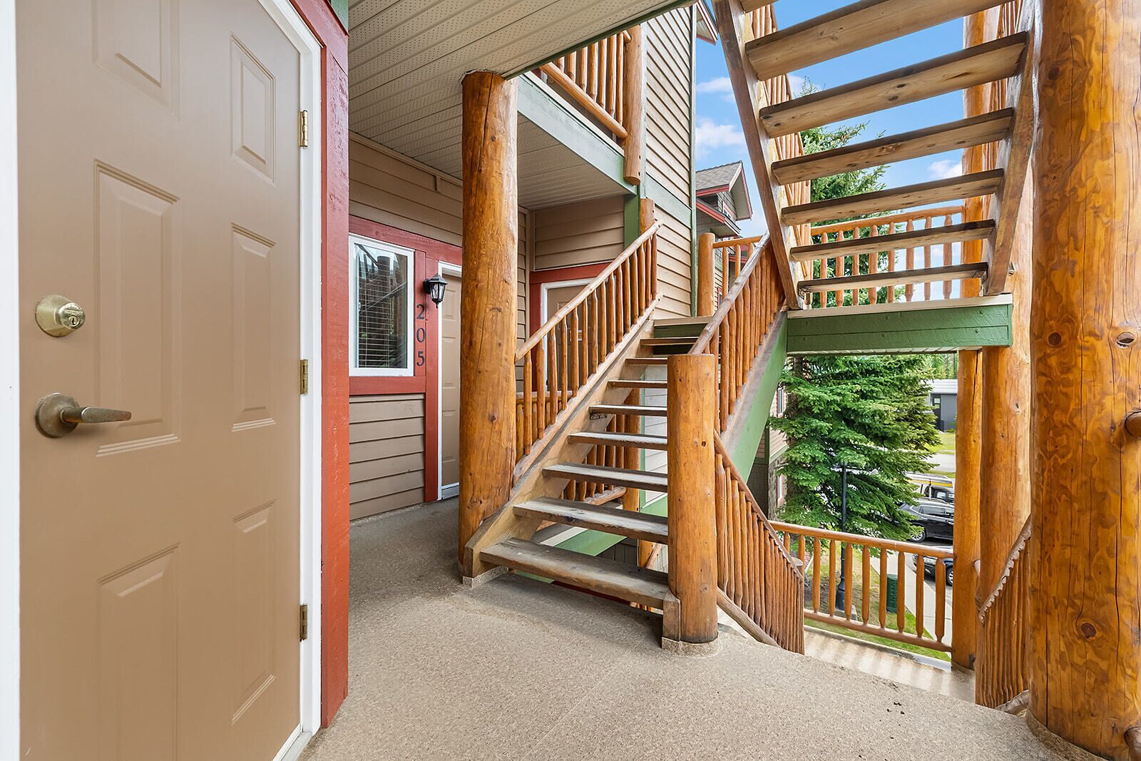 A wooden staircase leading to a balcony with a view of a tree and parked cars.