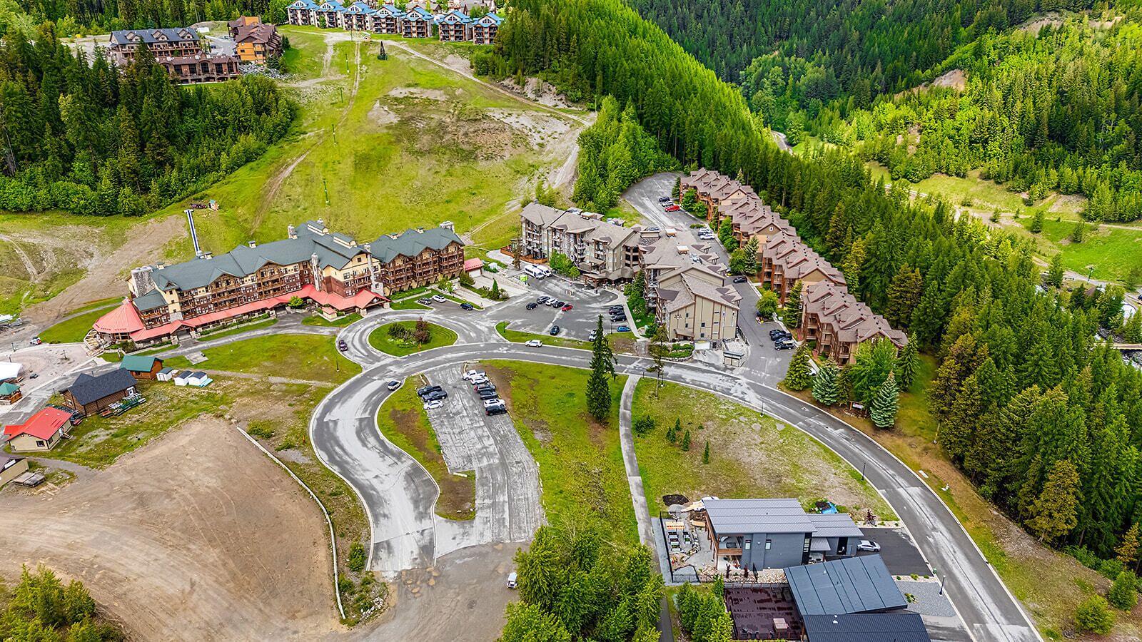 Vue aérienne d’un complexe hôtelier comprenant plusieurs bâtiments, une route sinueuse et une forêt environnante.