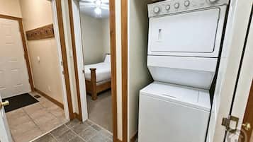 Une buanderie équipée d’un lave-linge et d’un sèche-linge superposés, une chambre adjacente et une porte donnant sur un autre espace.