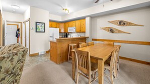 Een compacte keuken met houten kastjes, een centraal eiland en een eethoek met een houten tafel en stoelen.