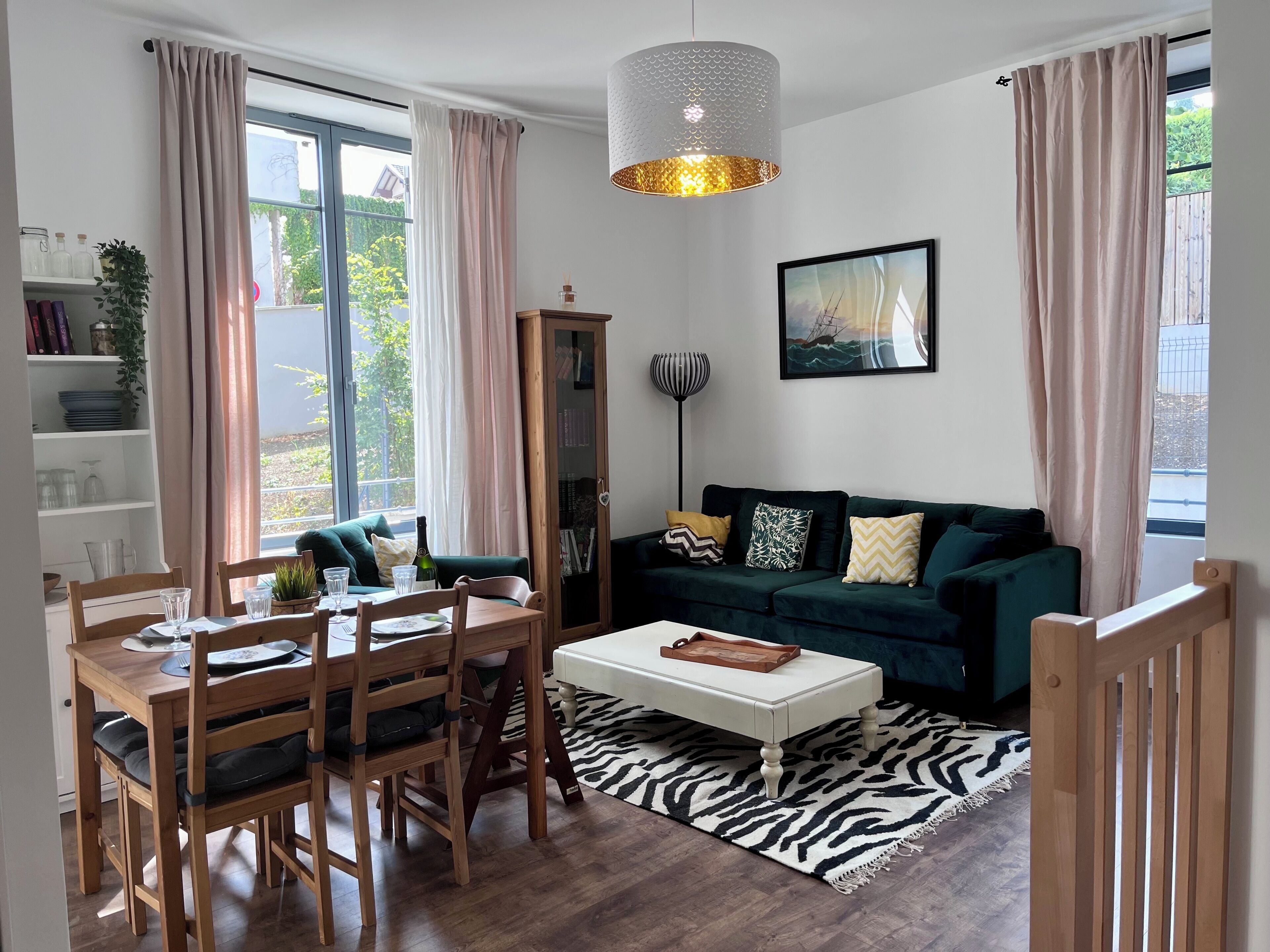 Een moderne woonkamer met een eethoek, een groene bank, een vloerkleed met zebraprint en een groot raam met gordijnen.