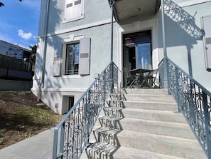 A building with a staircase leading to a door, a small outdoor seating area, and a fence. - Charming Apartment "La Montagne" for 4 Guests (Évian-les-Bains)