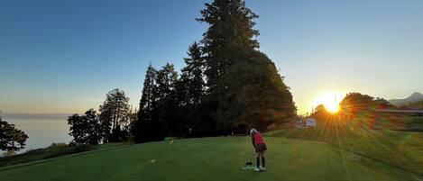 Una persona en un campo de golf con vistas al atardecer y árboles.