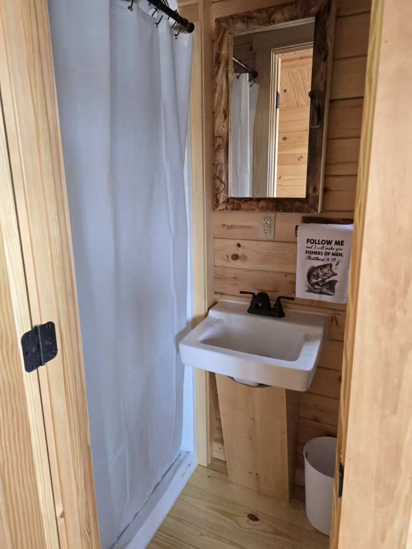 Bagno di una casetta in legno con tenda da doccia, lavandino e specchio.