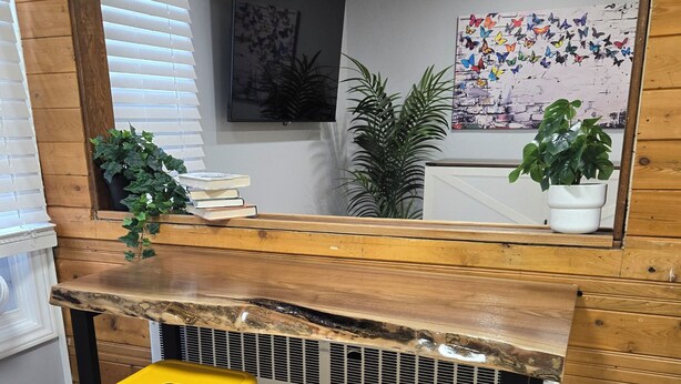 Un angolo cottura con piano in legno, due sgabelli gialli, una pianta in vaso e uno specchio fissato alla parete.