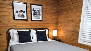 Una camera da letto con un letto, pareti in legno, due quadri incorniciati, una lampada da comodino e una finestra con persiane.