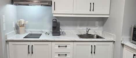 Una cocina con armarios blancos, un lavamanos de acero inoxidable y una campana extractora integrada.
