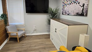 A living room with a TV mounted on the wall, a wooden cabinet, a chair, and a sofa.