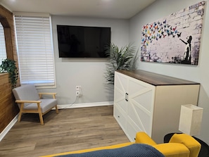 A living room with a TV mounted on the wall, a wooden cabinet, a chair, and a sofa.