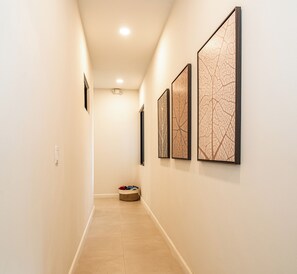 A hallway with three framed artworks on the wall, a basket with items on the floor, and a ceiling light. - Villa LaLa Land • 5 BR House with private pool (Jaco)
