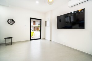 A spacious hallway with a dartboard, a small table, and a large flat-screen TV mounted on the wall. - Villa LaLa Land • 5 BR House with private pool (Jaco)