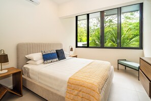 A bedroom with a bed, bedside tables, a bench, and a window with a view of greenery. - Villa LaLa Land • 5 BR House with private pool (Jaco)