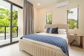 Een moderne slaapkamer met een groot bed, een balkon met uitzicht op groen en een raam met uitzicht op bomen.