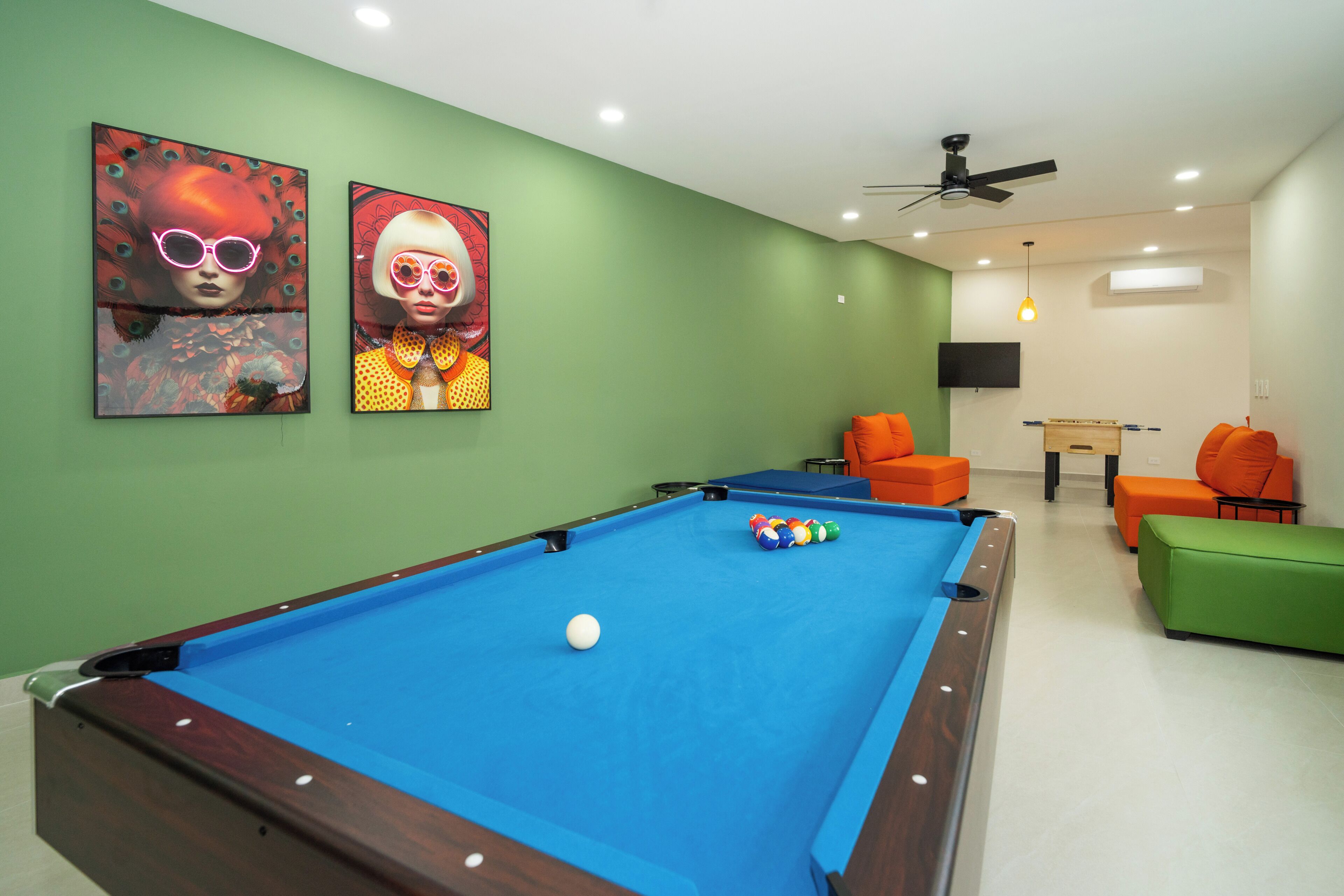 A pool table with balls, a ceiling fan, and two orange chairs.