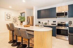 Een moderne keuken met een centraal eiland, krukken, roestvrijstalen apparatuur en een magnetron boven het aanrecht.