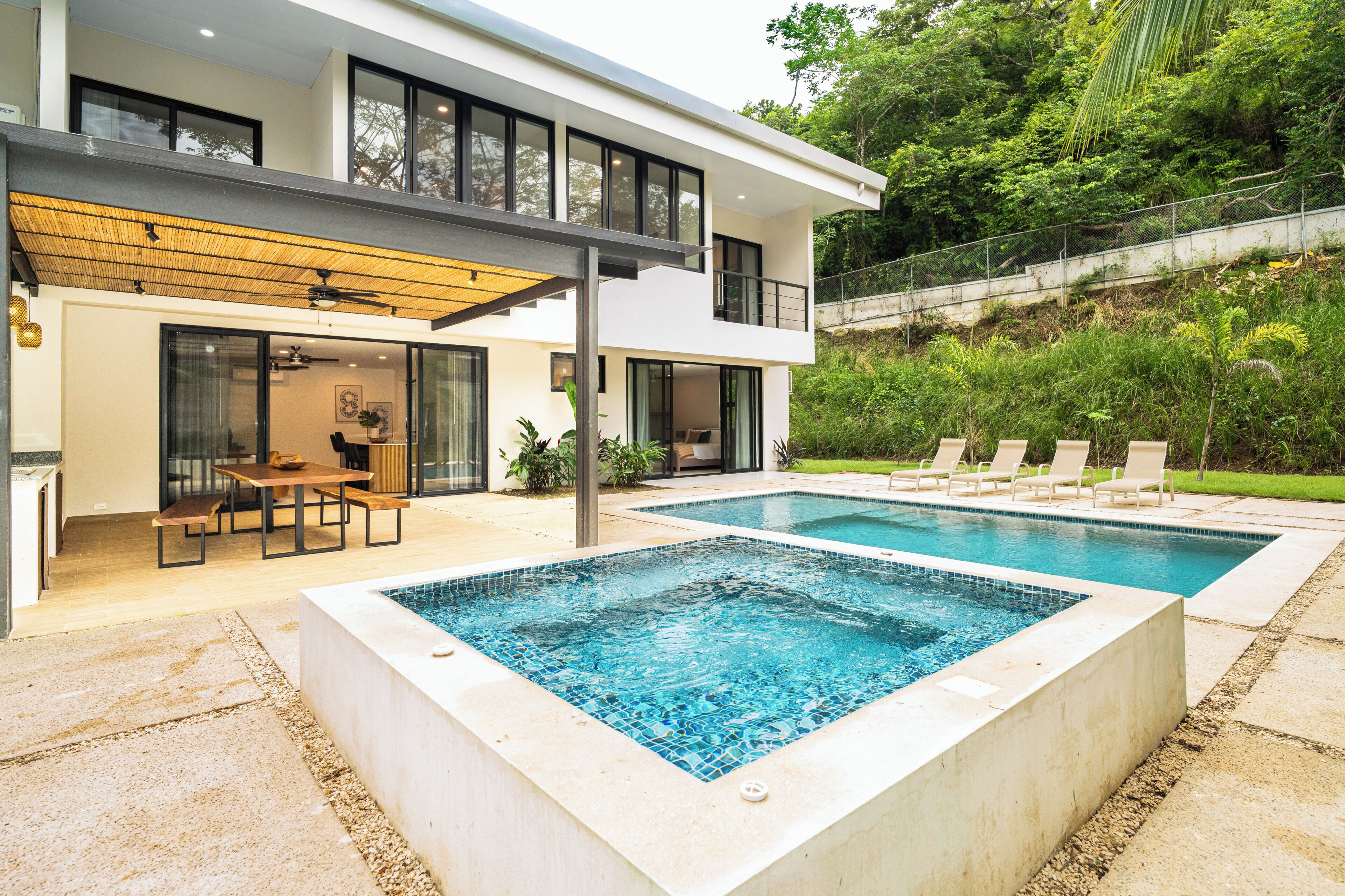 Una casa moderna de dos pisos con piscina, mobiliario exterior y un patio cubierto.