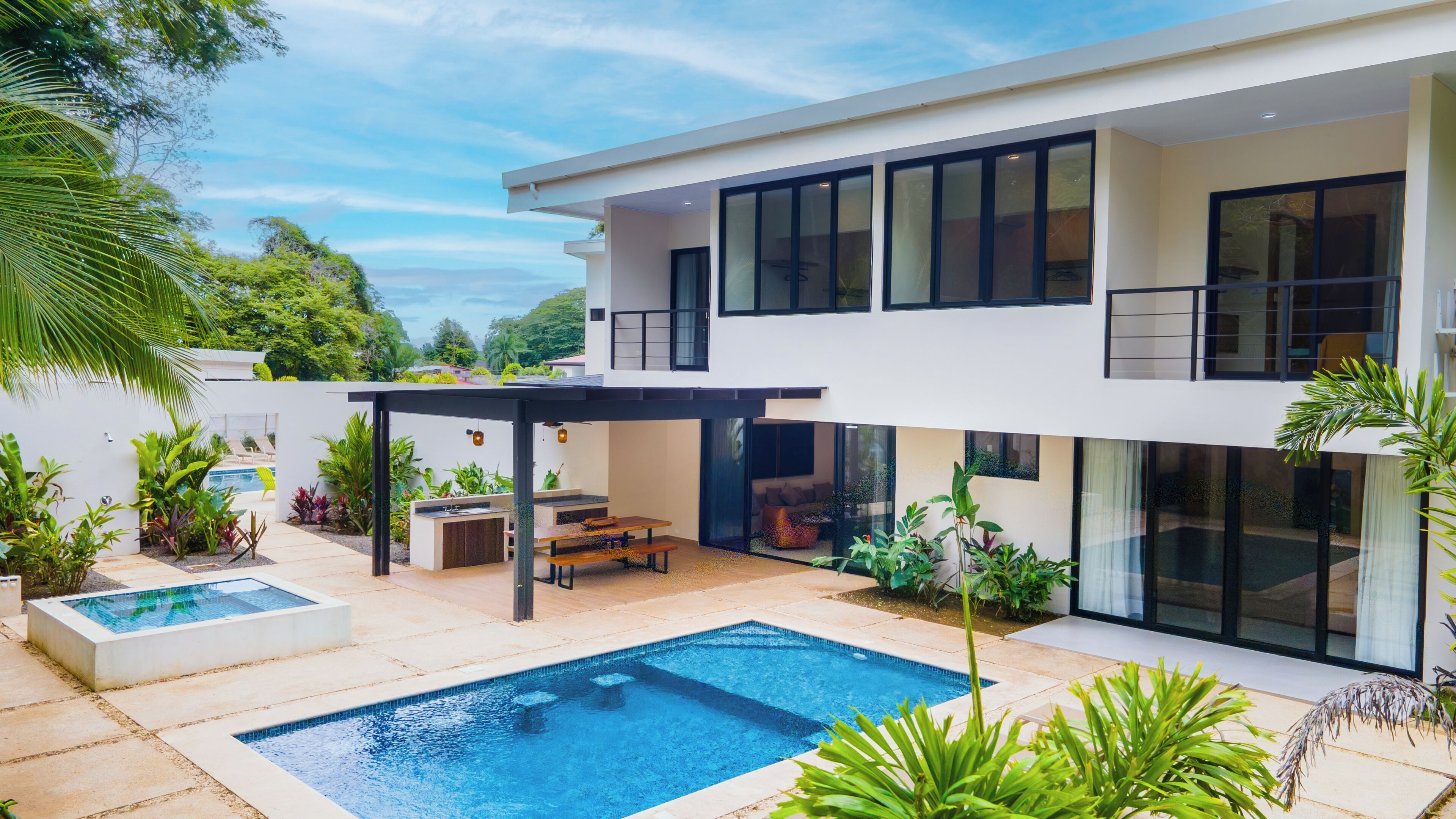 Une maison moderne à deux étages dotée d’une piscine, d’un espace extérieur aménagé et d’une végétation luxuriante.