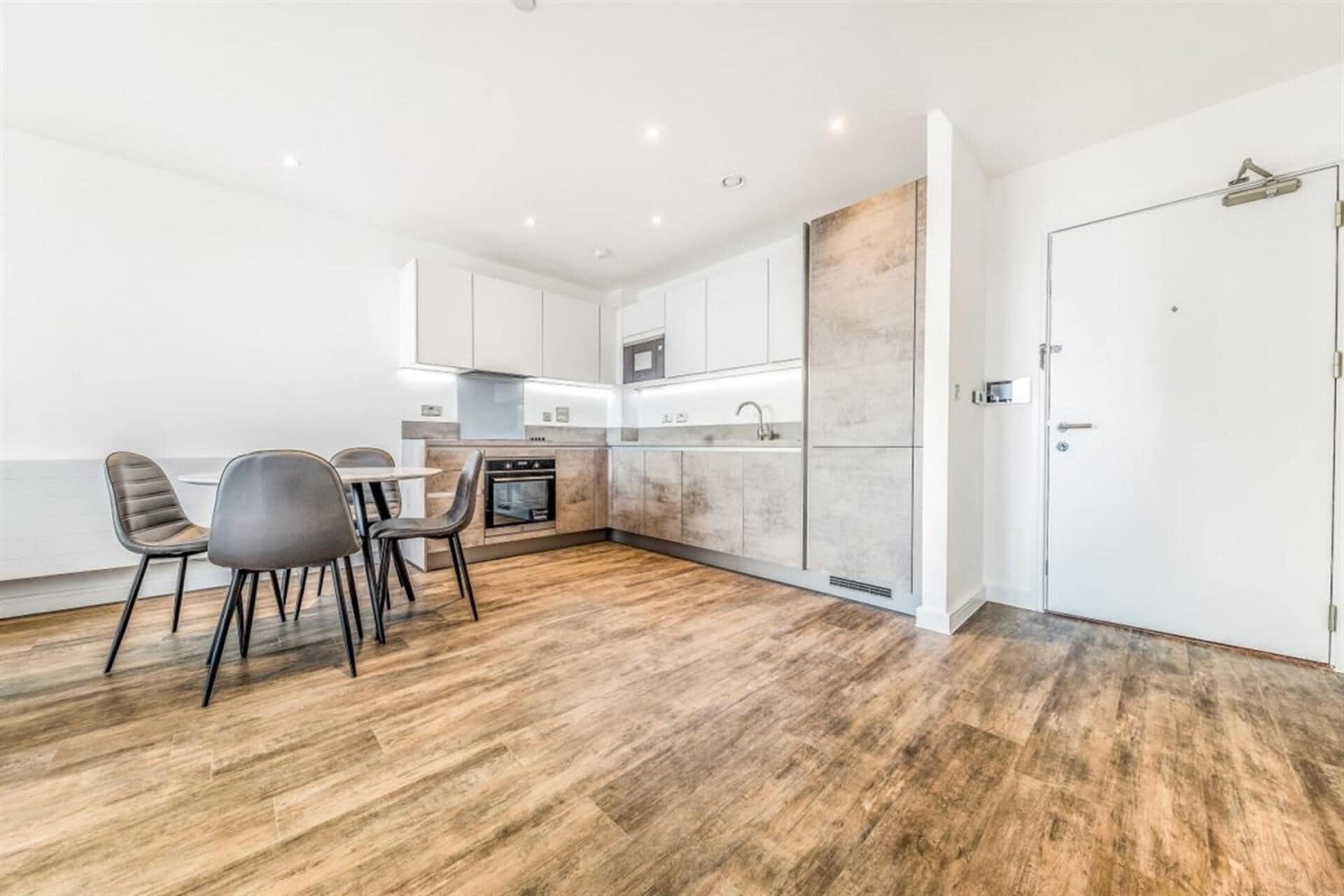 A modern kitchen with white cabinets, a built-in oven, and a dining area with two chairs.