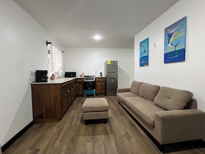 A compact living space with a kitchenette, a sofa, and two wall-mounted paintings. - Raul Villas  Hotel & Hostal  (Coxen Hole)