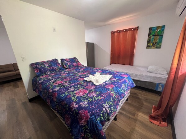 A bedroom with a floral bedspread, a single bed, a sofa, and a painting on the wall.