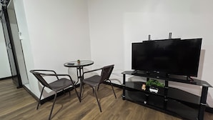 Una sala moderna con una televisión de pantalla plana, dos sillones, una mesita redonda y suelo de madera.