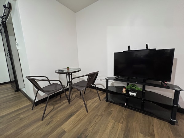 A modern living room with a flat-screen TV, two chairs, a small round table, and a wooden floor.