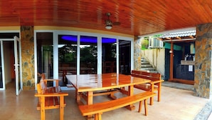 A covered outdoor dining area with a wooden table and benches, stone pillars, and a ceiling fan. - Monk Punta Fuego Beach House Nasugbu (Nasugbu)