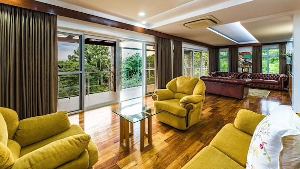 A spacious living room with a glass coffee table, yellow armchairs, a leather sofa, and a view of greenery through large windows. - Monk Punta Fuego Beach House Nasugbu (Nasugbu)