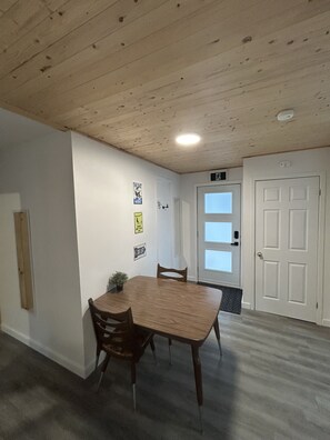 Ein Zimmer mit Holzboden, einer weißen Tür, einem Tisch mit Stühlen und an der Wand befestigten Schildern.