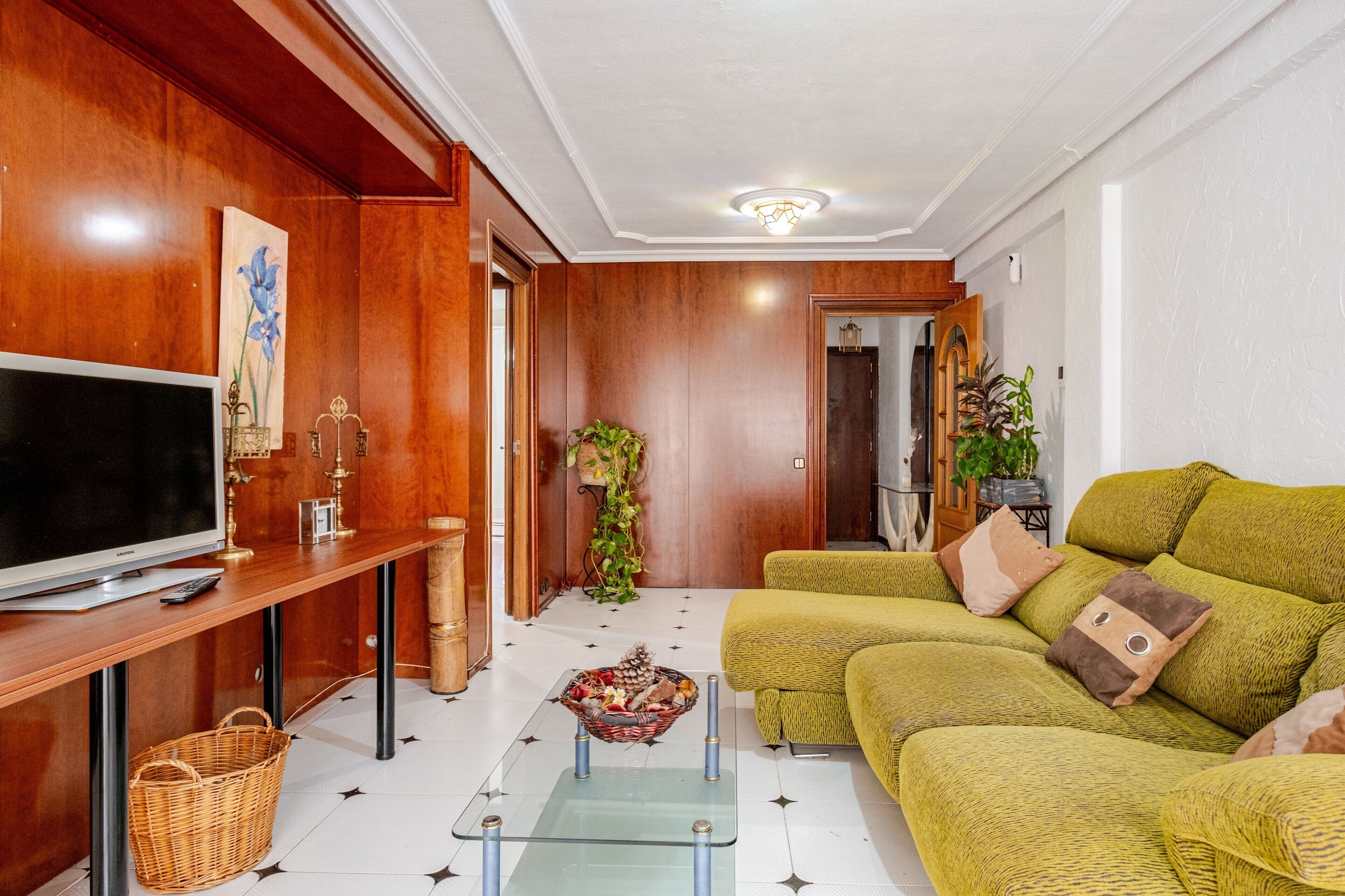 Een woonkamer met een televisie, een houten kast, een bank en een glazen salontafel.