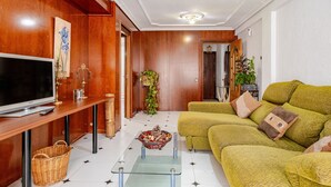 A living room with a television, a wooden cabinet, a sofa, and a glass coffee table.