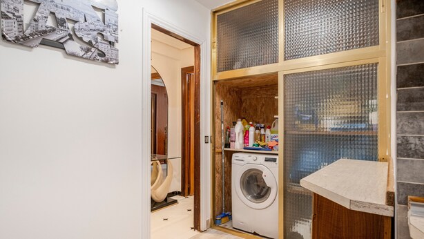 A laundry room with a washing machine, a drying rack, and a shelf with cleaning supplies.