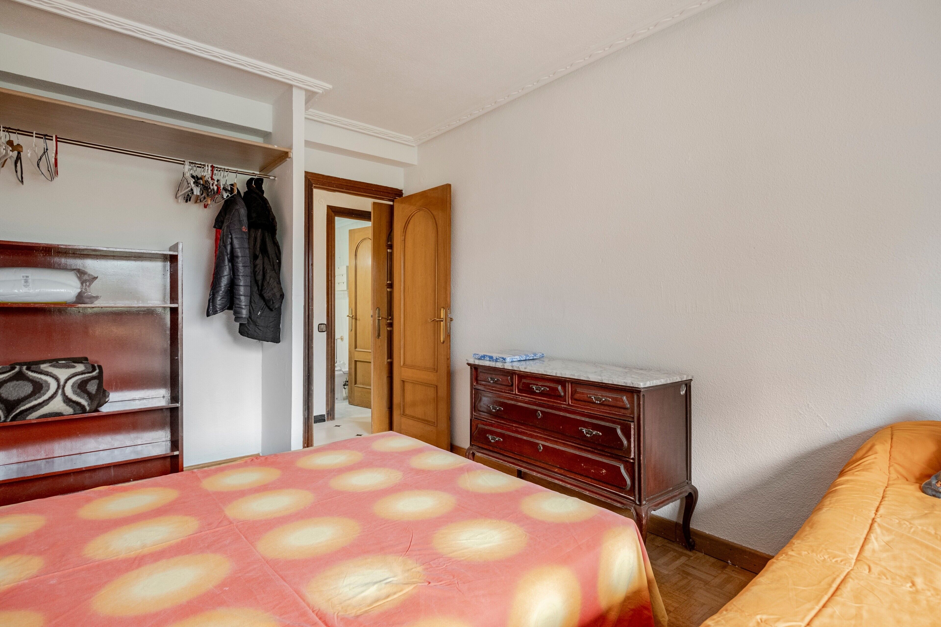 Een slaapkamer met een bed, een dressoir, een kledingkast en een deur naar een andere kamer.