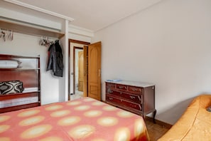 A bedroom with a bed, a dresser, a wardrobe, and a door leading to another room.