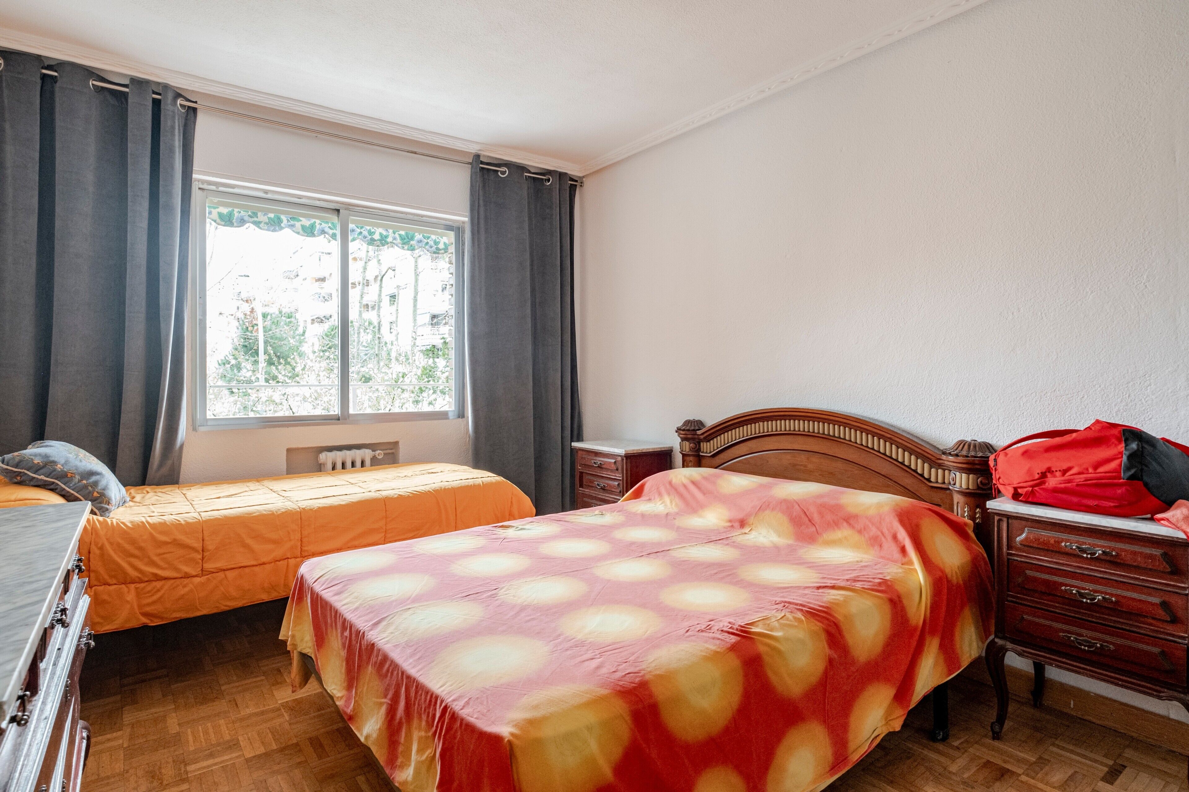 Ein Schlafzimmer mit zwei Betten, einem Schminktisch, einem Fenster mit Vorhängen und einer Heizung.