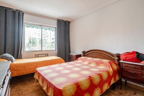 A bedroom with two beds, a dresser, a window with curtains, and a radiator.