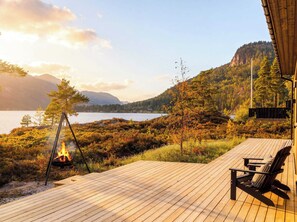 Una terraza de madera con un brasero, con vistas a un lago y montañas boscosas.