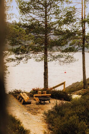 Un cadre idyllique au bord du lac, avec un banc en bois, des troncs d’arbres et une table en métal.
