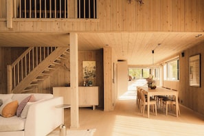 A spacious loft-style room with a wooden staircase, a dining area with a table and chairs, and a cozy seating area with a sofa and cushions.
