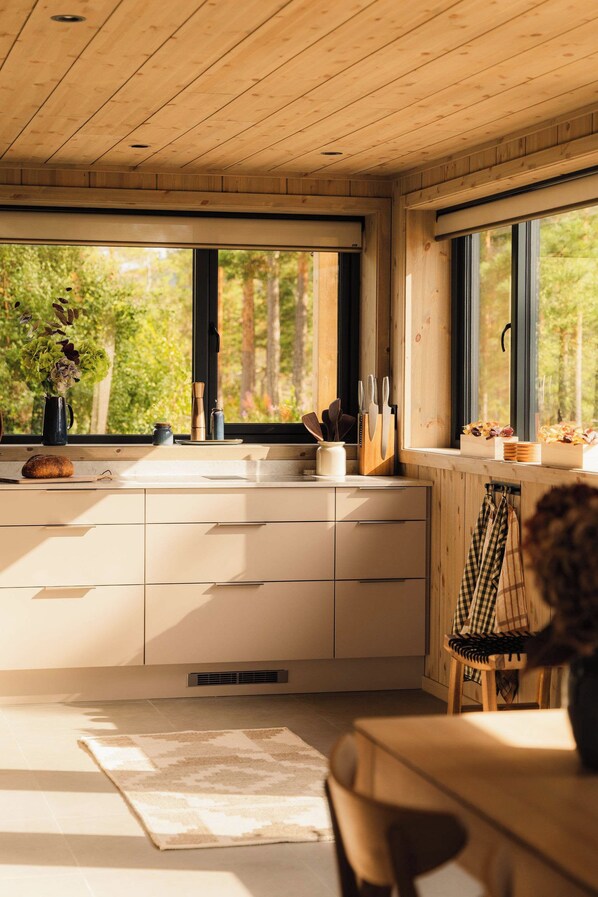 A modern kitchen with wooden cabinets, a large window, and a view of greenery outside.