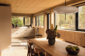 Una cocina moderna con armarios de madera, una mesa de comedor con sillas y un amplio ventanal con vistas a árboles.